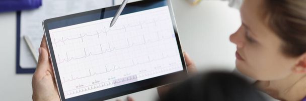 Close-up of doctor show digital tablet screen with heart cardiogram result to coworker. Examination of cardiovascular system. Medicine, cardiology concept - 写真・画像