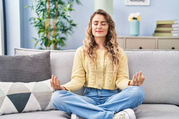Young woman doing yoga exercise sitting on sofa at home - Photo, image