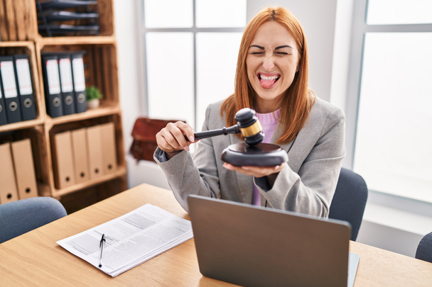 Young business woman using gavel sticking tongue out happy with funny expression.  - Photo, image