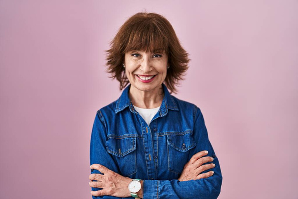 Middle age woman standing over pink background happy face smiling with crossed arms looking at the camera. positive person.  - Photo, Image