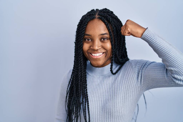 African american woman standing over blue background strong person showing arm muscle, confident and proud of power  - Foto, Bild