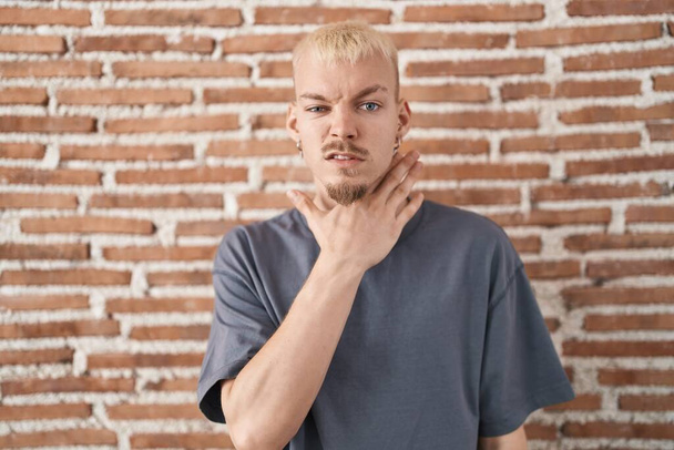 Young caucasian man standing over bricks wall cutting throat with hand as knife, threaten aggression with furious violence  - Foto, afbeelding