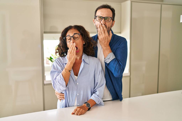 Middle age couple standing together bored yawning tired covering mouth with hand. restless and sleepiness.  - Foto, Bild