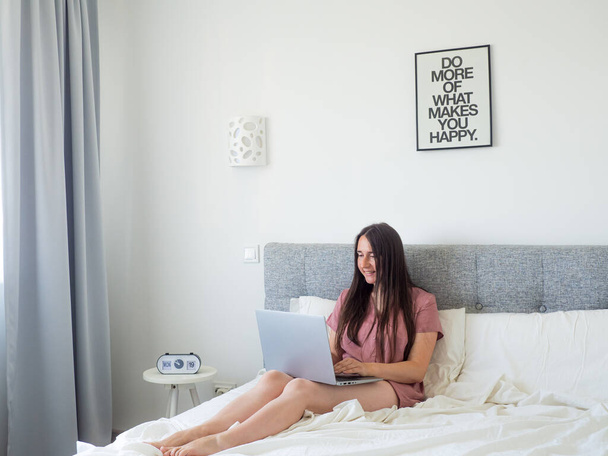 Woman working with laptop on the bed. Digital nomad and work from home concept. Young business woman working on computer, lying in the beautiful white and sunny bedroom. view with copy space - Foto, Bild
