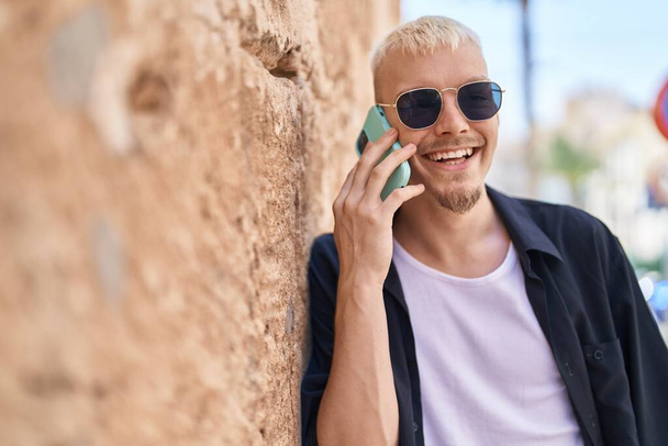 Nuori valkoihoinen mies hymyilee luottavainen puhuu älypuhelimeen kadulla - Valokuva, kuva