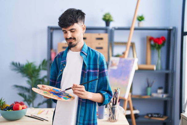 Young hispanic man artist holding paintbrush and palette at art studio - Foto, immagini