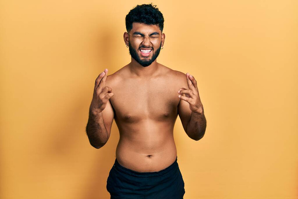Arab man with beard wearing swimwear shirtless gesturing finger crossed smiling with hope and eyes closed. luck and superstitious concept.  - Foto, Bild