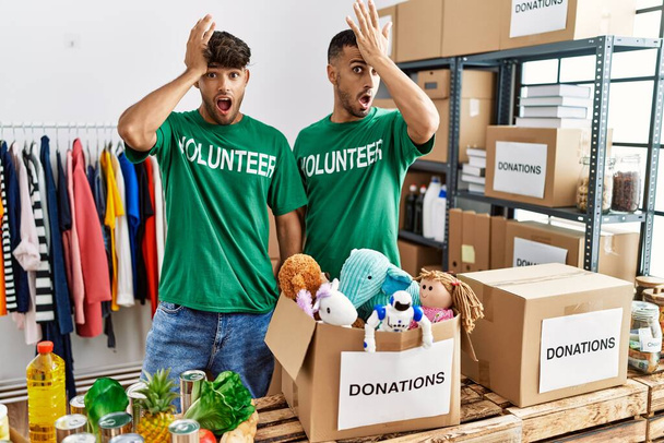 Jong homo paar dragen vrijwilliger t-shirt bij donaties staan verrast met de hand op het hoofd voor fout, herinner fout. vergeten, slecht geheugen concept.  - Foto, afbeelding