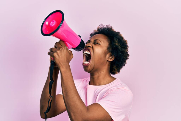Африканская американка с афро-волосами кричит с мегафоном на розовом фоне - Фото, изображение