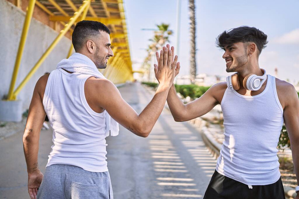 Δύο Ισπανοί άντρες χαμογελούν με αυτοπεποίθηση. Κόλλησαν πέντε με τα χέρια ψηλά στο δρόμο. - Φωτογραφία, εικόνα