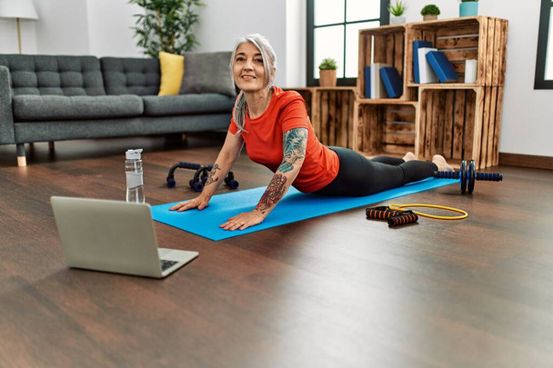 Middle age grey-haired woman smiling confident having online stretching class at home - Foto, Imagen