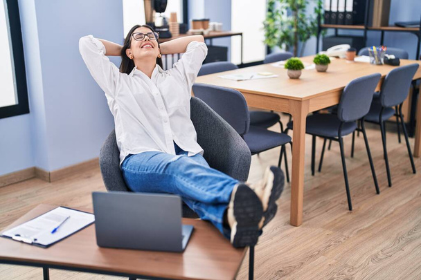 Trabajadora de negocios hispana joven relajada con las manos en la cabeza en la oficina - Foto, imagen