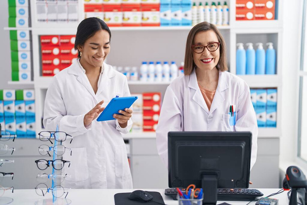 Two women pharmacist using computer and touchpad working at pharmacy - Photo, image