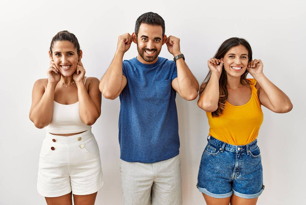 Een groep jonge Latijns-Amerikaanse mensen die met hun vingers over geïsoleerde achtergrond staan te glimlachen, grappig gebaar. auditieprobleem  - Foto, afbeelding