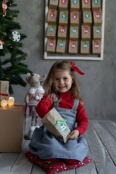 Adventskalender handgemacht für Kinder. glückliches Mädchen in lässiger Kleidung öffnet Basteltasche mit Bonbons mit Nummer, Weihnachten Kinder Fan, Winter Home Traditions Konzept - Foto, Bild