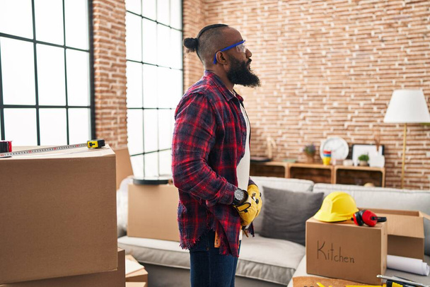 Hombre afroamericano que trabaja en la renovación del hogar mirando al costado, pose de perfil relajado con cara natural con sonrisa confiada.  - Foto, imagen
