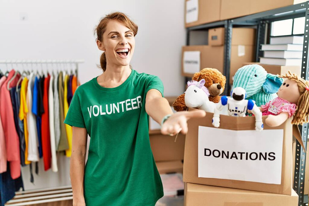 Beautiful caucasian woman wearing volunteer t shirt at donations stand smiling cheerful offering palm hand giving assistance and acceptance.  - Foto, imagen