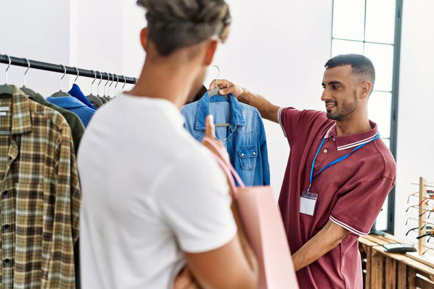 Молодий іспаномовний покупець, що показує одяг клієнту в магазині одягу
. - Фото, зображення