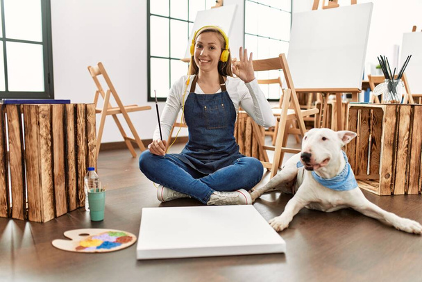 Caucasian young blonde woman at art studio doing ok sign with fingers, smiling friendly gesturing excellent symbol  - Foto, imagen