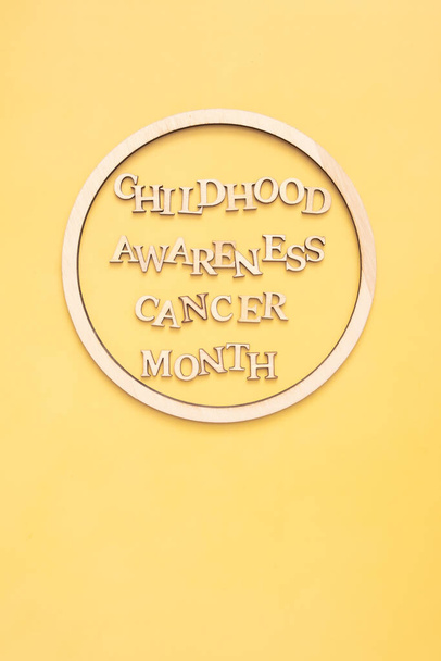 Childhood cancer awareness month text from wooden letters in round wooden frame on yellow background. Vertical format. - Photo, Image