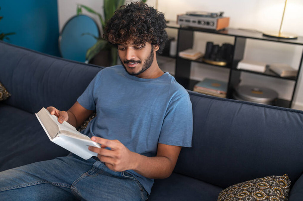 Reading a book. Curly-haired indian guy reading a book and looking involved - 写真・画像