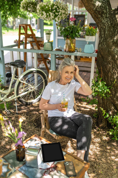 Κοκτέιλ στην αυλή. Μια ώριμη γυναίκα να κάθεται έξω και να πίνει το κοκτέιλ της - Φωτογραφία, εικόνα