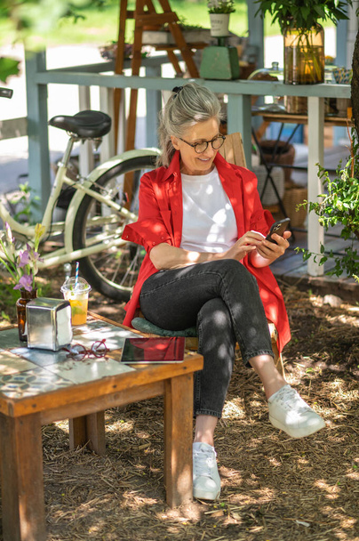 Leisure. A woman in red shirt sitting outside and spending time online - Φωτογραφία, εικόνα