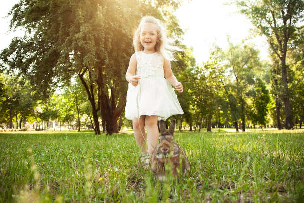 Little cute baby girl walking a pet rabbit, care and living with animal. Happy childhood, love of nature. - Photo, Image