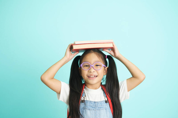 Kid students going to school, girl funny smiling, kid students girl with glasses hold books on her head, blue studio background, school concept. - Photo, image