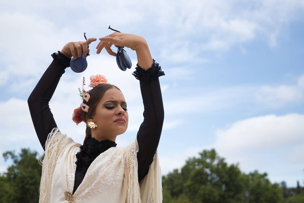 Portrait of young teenage girl in black dance dress, white shawl and pink carnations in her hair, dancing flamenco with castanets in her hands. Concept of flamenco, dance, art, typical Spanish dance. - Photo, Image