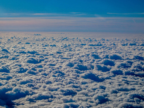 Cloudscape against a clear blue sky, group of dense white clouds covering the atmosphere, seen from an airplane in flight, sunny day with the horizon in the background. Space for text - Foto, Imagem