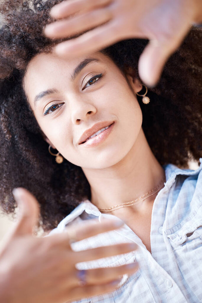 Beautiful young woman smiling and framing her face using her fingers from above. Happy hispanic woman with curly afro hair lying down creating frame around her face with hands and fingers. - Foto, Imagem