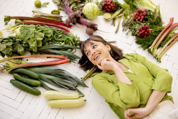 Портрет молодой веселой женщины с большим количеством свежих овощей, фруктов и зелени над головой, вид сверху. Концепция веганского питания и здорового образа жизни - Фото, изображение