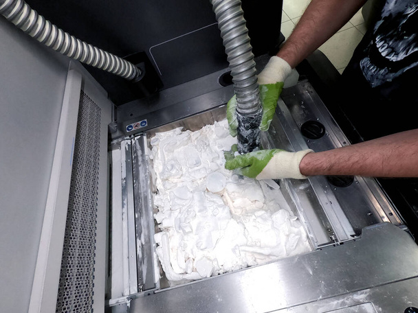 Человек, работающий с работающим пылесосом для очистки белого порошка от полиамида от модели, напечатанной на 3D принтере внутри 3D принтера. Очистка объектов, напечатанных на промышленном порошковом 3D принтере - Фото, изображение