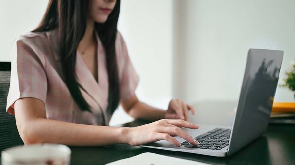 Przycięte zdjęcie pracującej kobiety wpisującej biznesową wiadomość e-mail, przeszukującej informacje na laptopie. - Zdjęcie, obraz