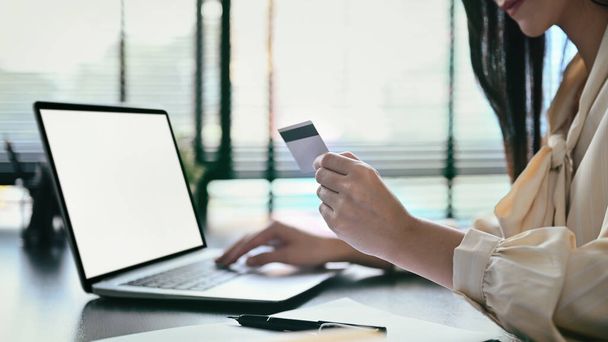 Młoda kobieta posiadająca kartę kredytową, dokonująca płatności przez Internet za pomocą laptopa. - Zdjęcie, obraz