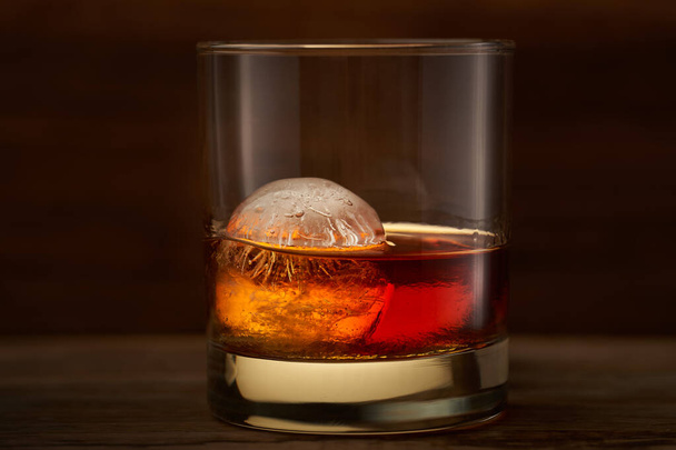 A glass of whisky with round big ice cube inside - Foto, Imagen