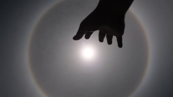 Aerial view of the sun with a circular rainbow surrounded by bright skies and white clouds with shadows of outstretched hands. Phenomenon, sun halo. Natural background in motion. - Felvétel, videó