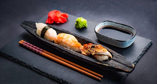 Sushi sashimi set with shrimps, ginger and soy sauce served with chopsticks and wasabi on black table. Traditional japanese meal with rice and seafood - Zdjęcie, obraz