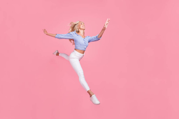 Full length photo of pretty sweet girl dressed blue top jumping high running empty space isolated pink color background. - Photo, image