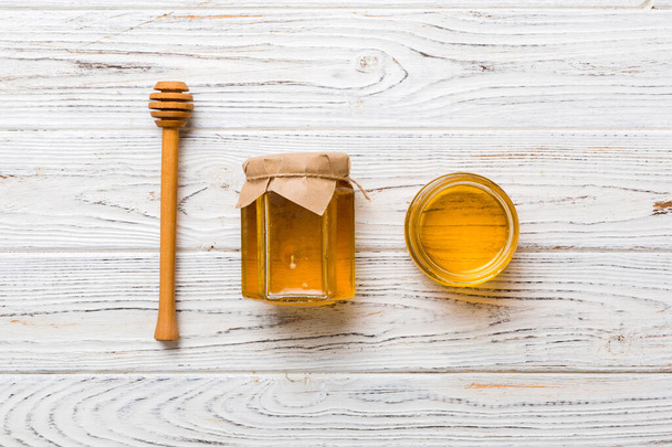 Glass jar of honey with wooden drizzler on colored background. Honey pot and dipper high above. Top view copy space. - Foto, afbeelding