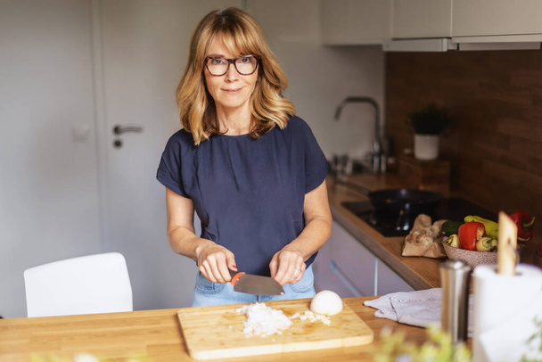 Shot of an attractive middle aged woman chopping vegetables in a kitchen at home.  - Foto, Bild