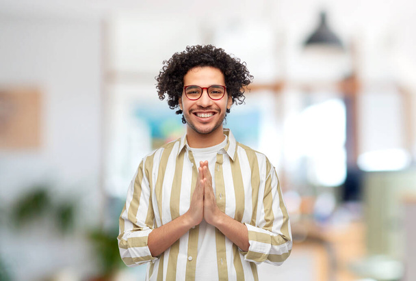 people, work and faith concept - happy smiling man in glasses making namaste gesture over office background - Фото, зображення