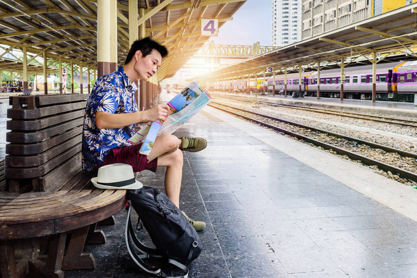 Koncept životní styl cestování nebo cesta: Mladý asijský muž cestovatel Při pohledu na mapu, zatímco čeká na vlak dorazí na nádraží. - Fotografie, Obrázek