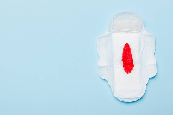 Women hygiene products or Sanitary pad with red feather on colored background. Pastel color. Closeup. Empty place for text. Female daily hygiene. - Photo, Image