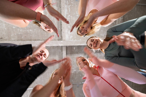 Group of six young motivated sporty girls wearing sports clothes standing together in a circle clapping their hands and cheering before or after a workout in fitness class. High quality photo - Photo, Image