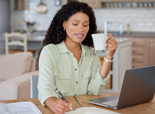 una joven escribiendo notas y tomando café mientras trabaja en un portátil en casa. - Foto, imagen