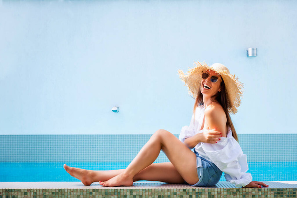 Shot of an attractive woman wearing straw hat and sunglasses while relaxing by the pool.  - Photo, Image