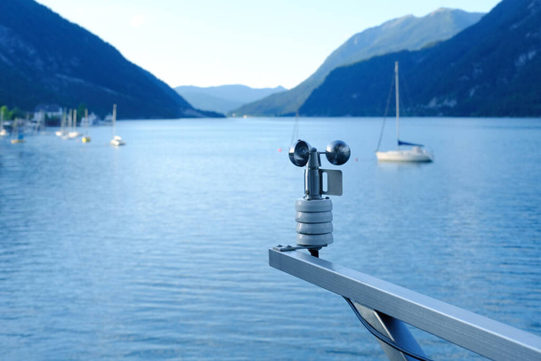 modern device anemometer over alpine lake controls parameters, meteorological equipment measures speed of movement of air masses, humidity levels, atmospheric pressure, wind strength and direction - Foto, Imagen