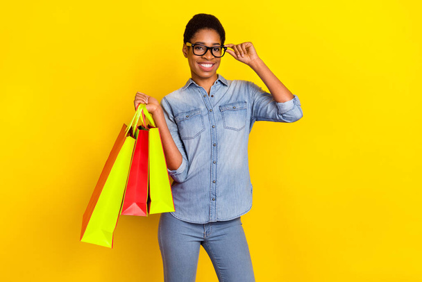 Portrait of satisfied person touch eyewear hold store mall packages isolated on yellow color background. - Φωτογραφία, εικόνα